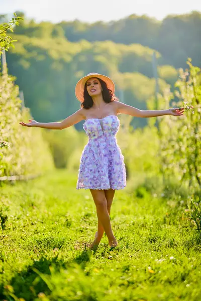 Arkaplanı bulanık, çiçek açmış bir elma bahçesinde güzel bir kadının vücut portresi.