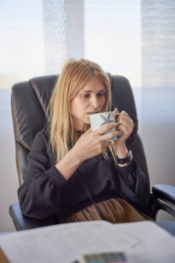 Elinde fincanla masada oturan orta yaşlı bir kadının portresi.