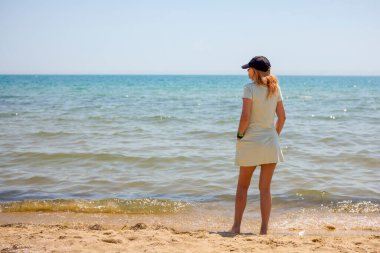 Dişi turist sahilde oturuyor ve bakıyor.