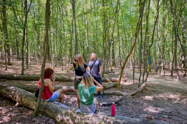 Bir grup insan ormanda yürüyüş yapıyor ve güneşli bir yaz gününde dinleniyorlar.