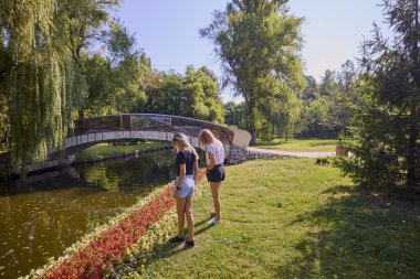 İki orta yaşlı kız kardeş bir yaz sabahını parkta dinlenerek ve eğlenerek geçiriyorlar..