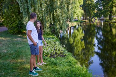 Baba ve kızı bir yaz sabahı göl kenarında parkta birlikte vakit geçiriyorlar doğanın tadını çıkarıyorlar..