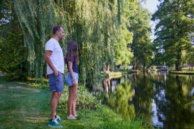 Baba ve kızı bir yaz sabahı göl kenarında parkta birlikte vakit geçiriyorlar doğanın tadını çıkarıyorlar..