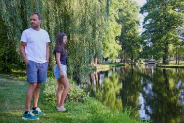 Baba ve kızı bir yaz sabahı göl kenarında parkta birlikte vakit geçiriyorlar doğanın tadını çıkarıyorlar..