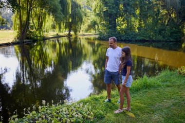 Baba ve kızı bir yaz sabahı göl kenarında parkta birlikte vakit geçiriyorlar doğanın tadını çıkarıyorlar..