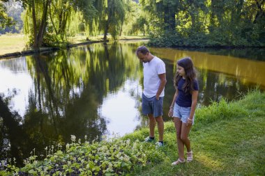 Baba ve kızı bir yaz sabahı göl kenarında parkta birlikte vakit geçiriyorlar doğanın tadını çıkarıyorlar..