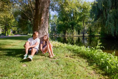 Baba ve kızı bir yaz sabahı göl kenarında parkta birlikte vakit geçiriyorlar doğanın tadını çıkarıyorlar..