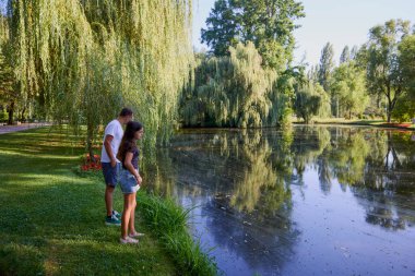 Baba ve kızı bir yaz sabahı göl kenarında parkta birlikte vakit geçiriyorlar doğanın tadını çıkarıyorlar..