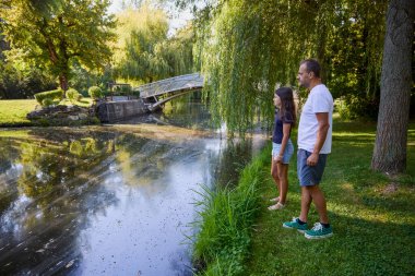 Baba ve kızı bir yaz sabahı göl kenarında parkta birlikte vakit geçiriyorlar doğanın tadını çıkarıyorlar..