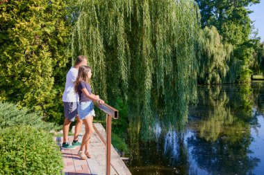Baba ve kızı bir yaz sabahı göl kenarında parkta birlikte vakit geçiriyorlar doğanın tadını çıkarıyorlar..