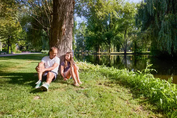 Baba ve kızı bir yaz sabahı göl kenarında parkta birlikte vakit geçiriyorlar doğanın tadını çıkarıyorlar..