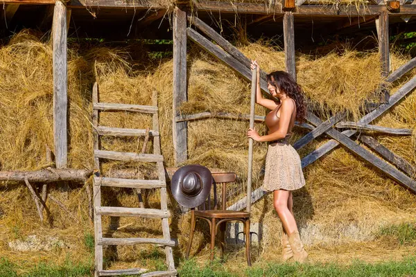 Kır kıyafetleri içinde güzel bir kadın ve saman ambarının yanında şapka, köy konsepti..