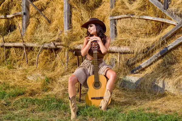 Kır kıyafetleri içinde güzel bir kadın ve saman ambarının yanında şapka, köy konsepti..