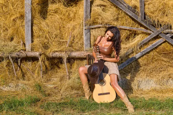 Kır kıyafetleri içinde güzel bir kadın ve saman ambarının yanında şapka, köy konsepti..