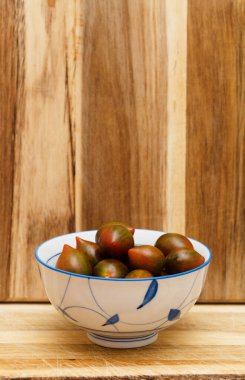 Small dark red-brown-green tomatoes in a bowl clipart