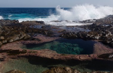 Gran Canaria, kuzey kıyısı, Puertillo de Banaderos çevresindeki kayalıklar okyanus dalgalarından korunan volkanik kaya bariyerleriyle korunuyor.