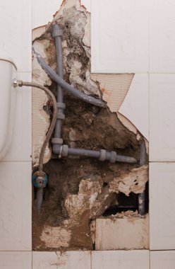 Kırık kiremitli banyo duvarı, plastik su boruları açıkta.