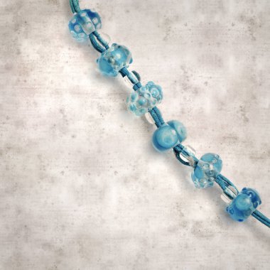 desenli eski kağıt arka plan, kare, mavi ve şeffaf cam boncuklardan oluşan basit bir kolye