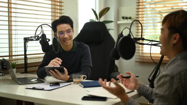 Yoğunlaştırıcı mikrofonun önünde oturan iki mutlu podcaster modern stüdyolarındaki kanalları için konuşmaları kaydediyor..