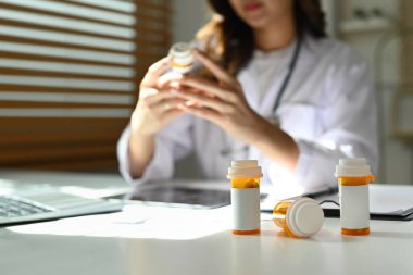 Beyaz masada boş etiketli ilaç şişelerine ve arka planda oturan kadın doktorlara yakından bakın..