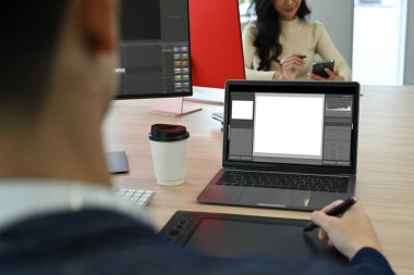 Yaratıcı iş yerinde oturan ve dizüstü bilgisayardaki fotoğrafları düzelten erkek fotoğraf editörlerinin omuz üstü görüntüsü..