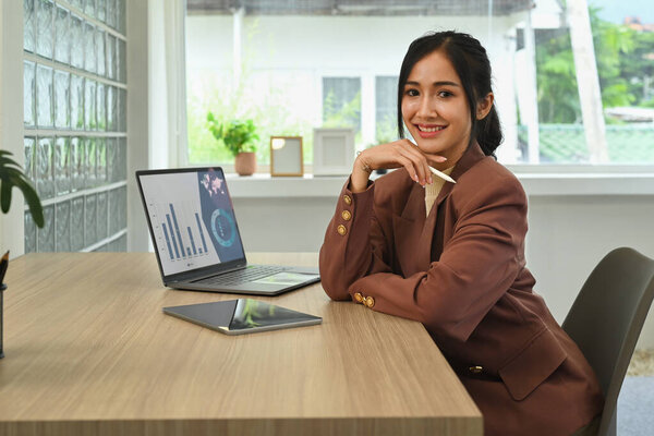 Successful young business entrepreneur in stylish suit sitting her workplace and smiling to camera.