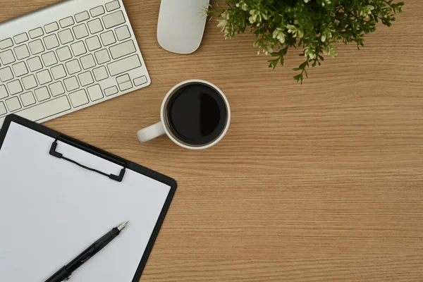 stock image Top view of wireless keyboard, coffee cup, clipboard and potted plant on wooden working desk.