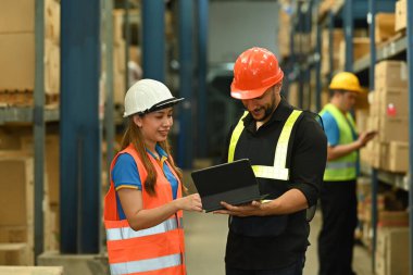 Genç işçiler raflarla dolu perakende deposunun arasında beklerken tabletteki sipariş detaylarını kontrol ediyorlar..