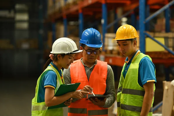 Middle aged male manager and young worker in hardhats and jackets using digital tablet for checking stock and order details.