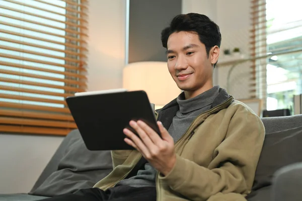 图片中 一个微笑的男人一边在电脑上观看视频 一边在家里的沙发上放松 — 图库照片