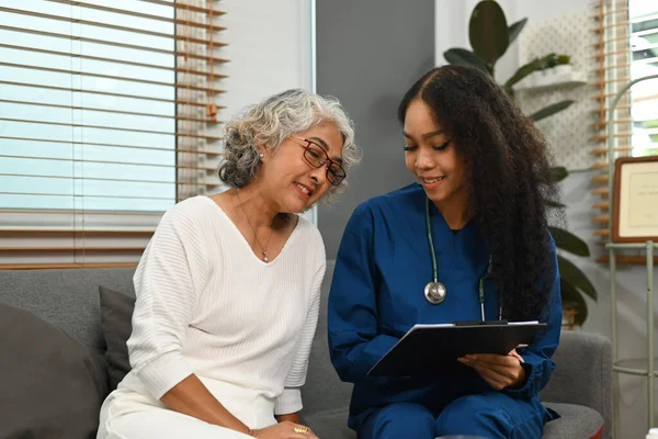 Attentive female doctor holding digital tablet and explaining medicine dosage to elder woman. Home health care service concept.
