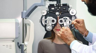 Optik fosforopterden bakan genç bir kadın, klinikte uzman bir optometrist ile göz görüşünü kontrol ediyor..