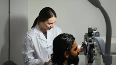 Beyaz önlüklü kadın göz doktoru özel tıbbi aletle hastayı muayene ediyor..