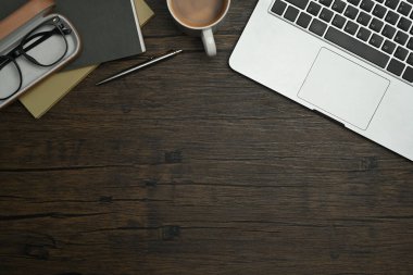 Dizüstü bilgisayarın, gözlüklerin, kahve fincanının ve kırsal ahşap masanın üstündeki defterlerin en üst görüntüsü..