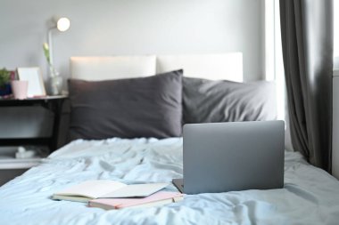 Dizüstü bilgisayar ve dizüstü bilgisayarlar yatağın üzerinde pencerenin yumuşak ışığıyla.