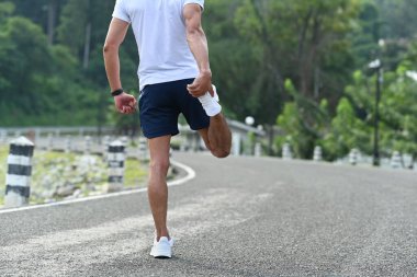 Sporcunun bacağını esnetip sabah antrenmanına hazırlandığı arka manzara. Sağlıklı yaşam tarzı ve sağlık kavramı.