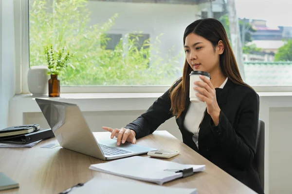 アジアの女性オフィスの労働者はコーヒーを飲み 彼女のラップトップコンピュータ上のビジネス電子メールをチェック — ストック写真