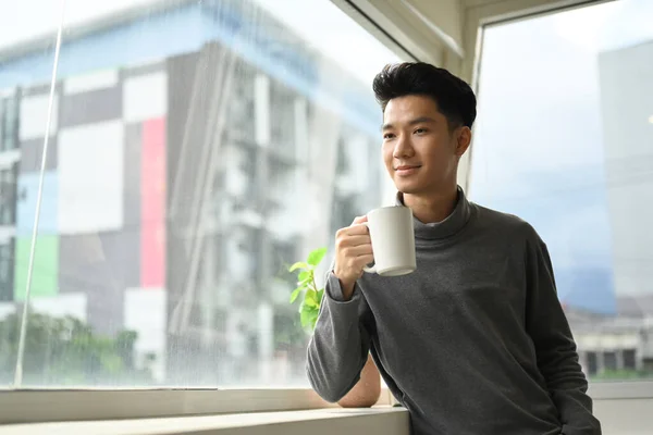 Όμορφος Ασιατικό Αρσενικό Πίνοντας Καφέ Στέκεται Κοντά Στο Παράθυρο Του — Φωτογραφία Αρχείου