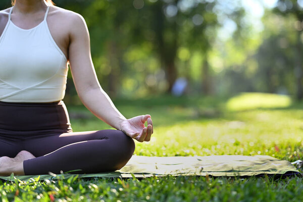 Image of yogi woman practicing yoga, meditating, doing Ardha Padmasana exercise in the park on a sunny summer day.
