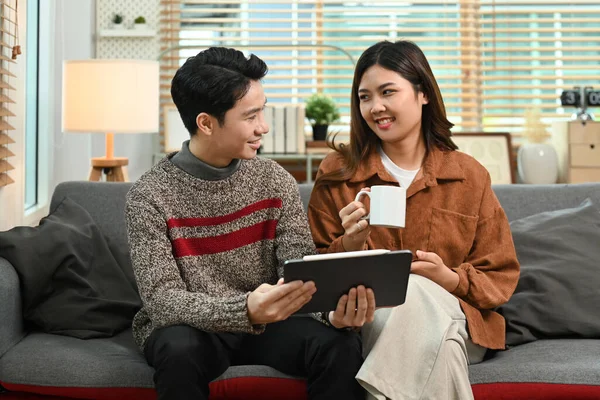 Pleasant young asian couple relaxing on couch and enjoy browsing wireless internet on digital tablet.
