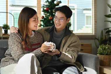 Rahat genç bir çift rahat koltukta oturuyor, parlak bir kış sabahı sıcak çikolata içmenin tadını çıkarıyorlar..