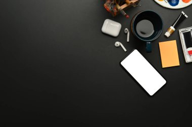 Akıllı telefonu, kulaklığı, kahve fincanı, boya ve paleti olan bir sanatçı. Kopyalama alanı olan üst görünüm.