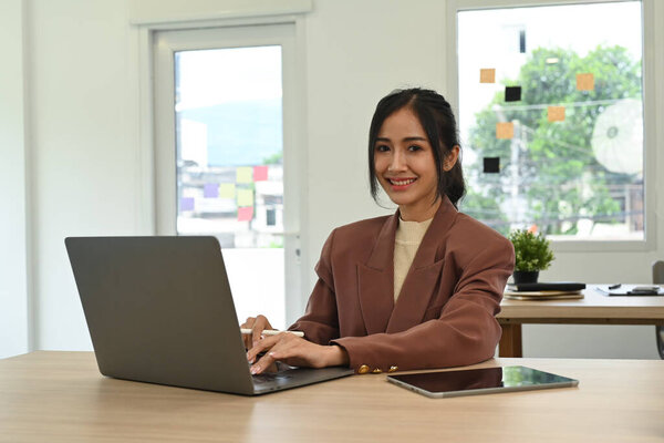 Stylish beautiful manager using laptop computer on wooden desk at modern office.
