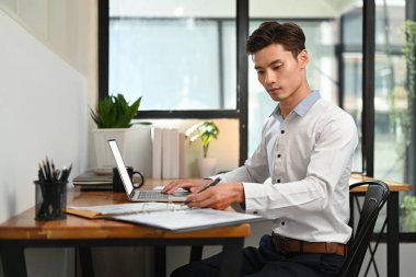 Laptop kullanan yakışıklı bir girişimci, küçük işletmesini evden yönetiyor..