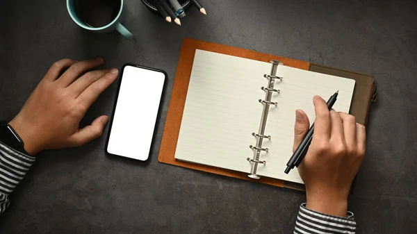 stock image Overhead view of businessman using mobile phone and making notes on notepad. Blank screen for your advertise text.