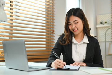 İnternette çalışan güzel Asyalı kadın yatırımcı dizüstü bilgisayardaki finansal çevrimiçi verileri analiz ediyor..