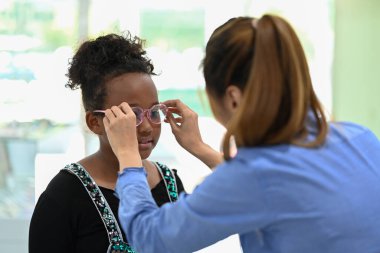 Optik mağazasında yeni gözlükleri optometrist ile test eden tatlı küçük bir kız. Görme ve görme konsepti.