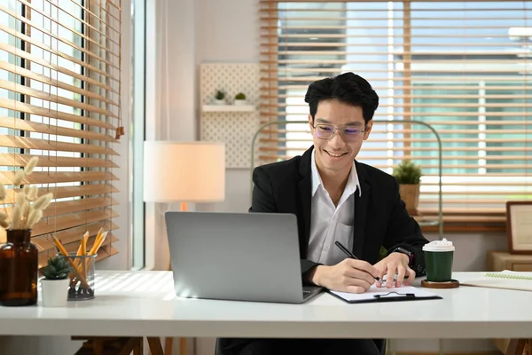 微笑的男人看着笔记本电脑 在剪贴板上记笔记 开始创业 — 图库照片
