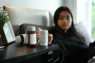 Genç bir kadın semptomları azaltmak için komodinden ilaç alıyor. Tıp, farmakoloji, sağlık hizmetleri kavramı.