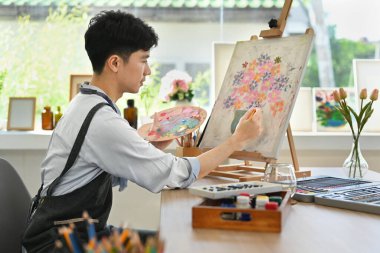 Rahat bir sanat atölyesinde sehpada suluboya resim yapan memnun bir adam. Boş zaman aktivitesi ve yaratıcı hobi konsepti.